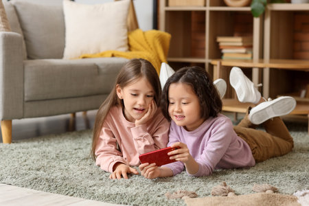 Cute girls watching cartoons on mobile phone at homeの写真素材