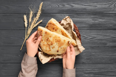 Female hands with wicker basket, pieces of tasty lavash and wheat spikelets on gray wooden...