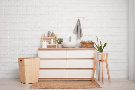Houseplants, cosmetic products and wicker basket with clean towels on modern sink in bathroom