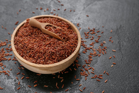 Wooden bowl with raw brown rice and scoop on black grunge backgroundの写真素材