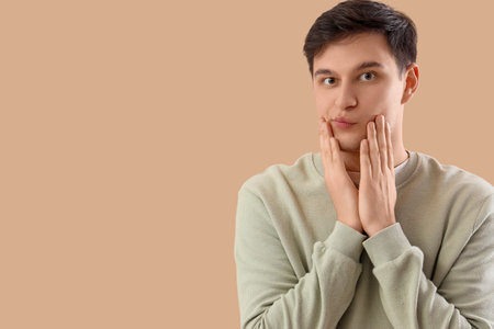 Young man doing face building exercise on beige backgroundの写真素材