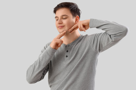 Young man doing face building exercise on light backgroundの写真素材