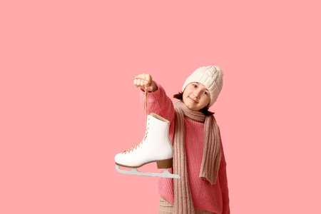 Cute little girl in winter clothes holding ice skate on pink backgroundの写真素材
