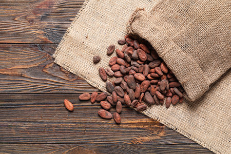 Bag with cocoa beans and burlap fabric on wooden background