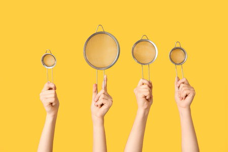 Female hands with sieves on yellow background