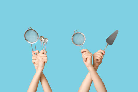 Female hands holding sieves with cake spatula and measuring spoons on blue background