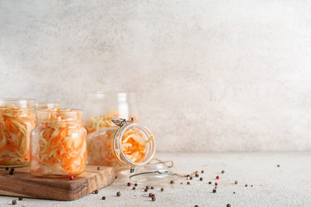 Jars of sauerkraut and scattered peppercorns on table against gray background. Closeupの写真素材