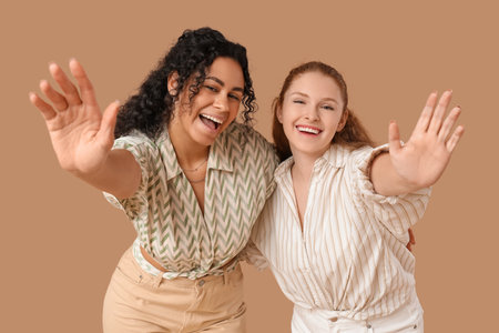 Beautiful young happy female friends waving hands on beige backgroundの写真素材