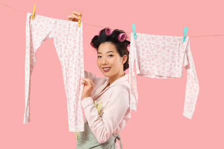 Happy young Asian woman with hanging laundry and clothespins on pink backgroundの写真素材