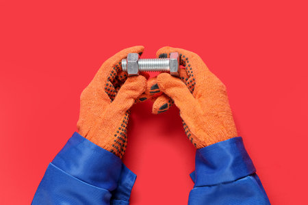 Mechanic's hands holding bolt with nut on red backgroundの写真素材