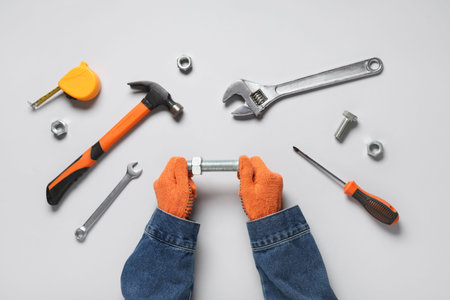 Mechanic's hands with bolt and tools on gray background