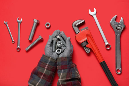 Mechanic's hands with bolts, nuts and tools on red backgroundの写真素材