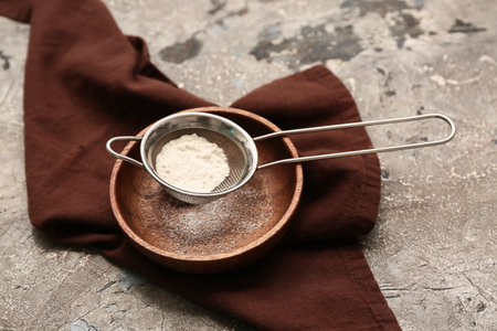 Metal sieve with flour in wooden plate and napkin on grunge backgroundの写真素材