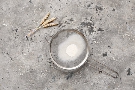 Metal sieve with flour and spikelets on grunge background