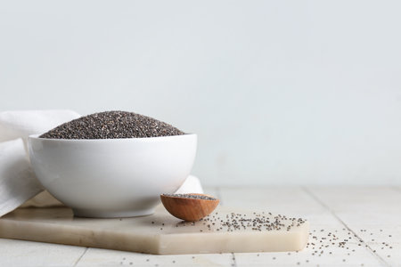 Bowl and wooden spoon with chia seeds on white tile tableの写真素材