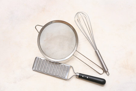 Metal sieve, grater and whisk on light background