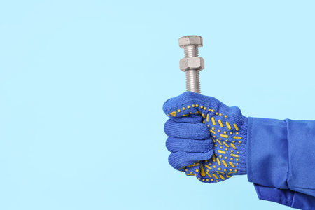 Mechanic's hand holding bolt with nut on blue backgroundの写真素材
