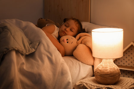 Cute little girl with knitted toy bunny sleeping in bedroom at nightの写真素材