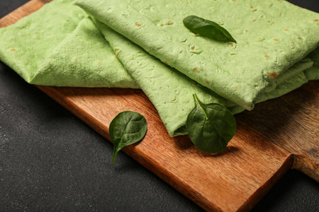 Wooden board with green lavash and spinach on black backgroundの写真素材