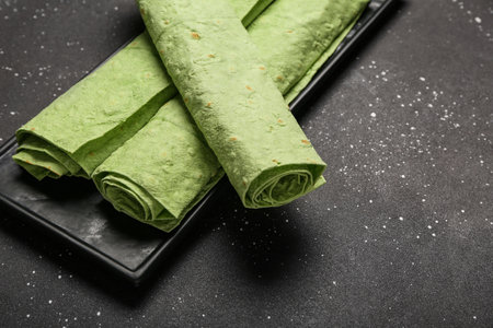 Plate with rolled green lavash on black grunge backgroundの写真素材