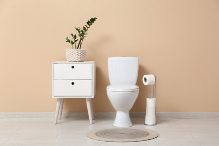 Interior of restroom with toilet bowl, bedside table and houseplant near beige wallの写真素材