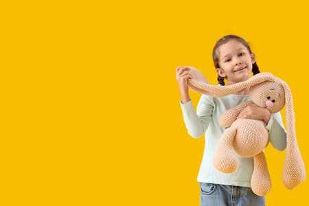 Cute little girl with knitted toy bunny on yellow backgroundの写真素材