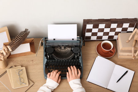 Female author typing on vintage typewriter at table in office, top view