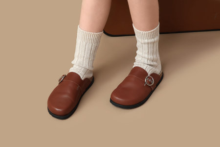 Teenage girl in clogs on beige background, closeup
