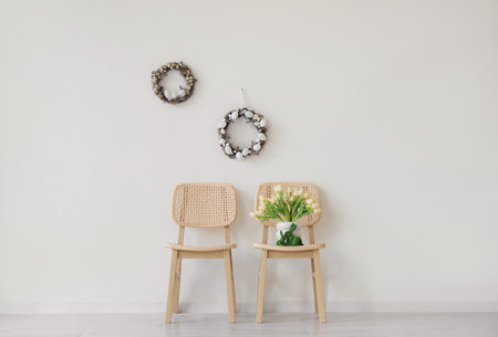 Chairs with tulips and Easter wreaths on light wall in roomの写真素材