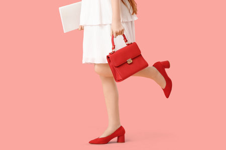 Stylish teenage girl in red shoes with bag and magazine on pink backgroundの写真素材