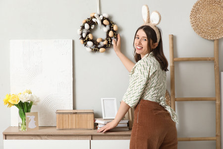 Young woman with Easter wreath on light wall at home