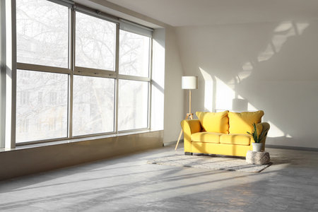 Yellow sofa with lamp and plant near light wall in big roomの写真素材
