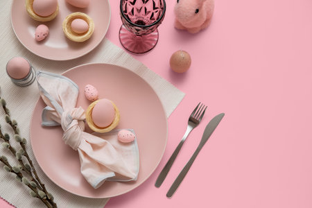 Beautiful table setting with Easter eggs, toy bunny and pussy willow branches on pink backgroundの写真素材