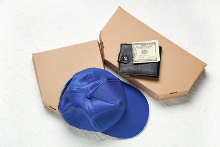 Courier's cap with wallet, money and cardboard boxes on white grunge background