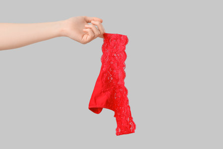 Woman holding red lace panties on gray backgroundの写真素材