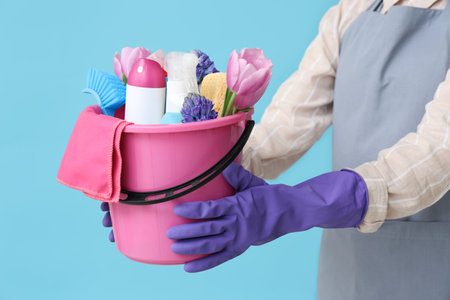 Female janitor with cleaning supplies and spring flowers on blue background, closeupの写真素材