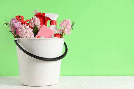 Cleaning supplies with spring flowers on table against green backgroundの写真素材
