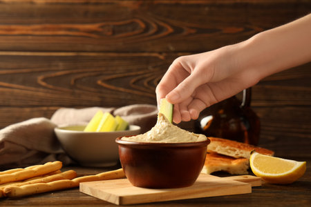 Woman eating delicious hummus with cucumber on wooden background