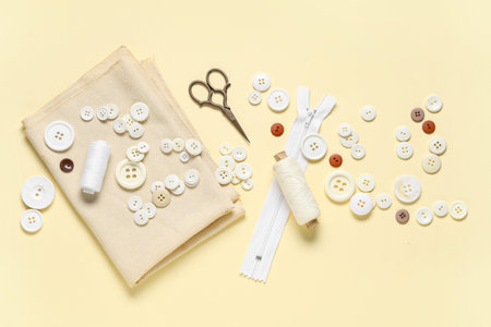 Different white buttons with sewing supplies and fabric sample on yellow background