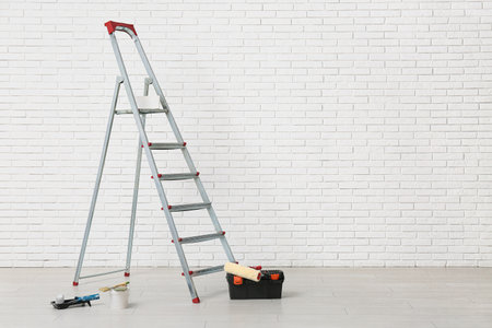 Stepladder with painting tools near white brick wall in roomの写真素材