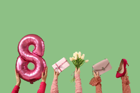 Female hands with figure 8 made of balloon, flowers, gift box and stylish accessories on green background. International Women's Day celebrationの写真素材
