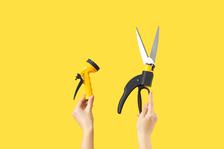 Female gardener holding spray gun with secateurs on yellow background
