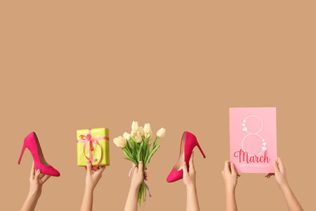 Female hands with gift box, flowers, greeting card and stylish high heels on beige background. International Women's Day celebrationの写真素材