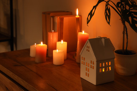 House shaped holder with burning candles, plant and books on shelf in dark room, closeupの写真素材