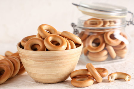 Wooden bowl and jar of tasty bagels on light background