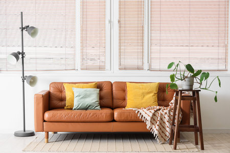 Interior of light living room with brown sofa, lamp and plant