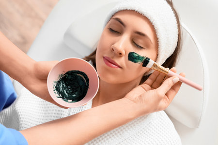 Cosmetologist applying spirulina mask onto woman's face in beauty salon, closeupの写真素材