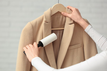 Woman cleaning coat with lint roller at home, closeupの写真素材