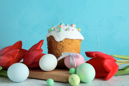 Tulip flowers, board, Easter eggs and cake on gray table near blue wall
