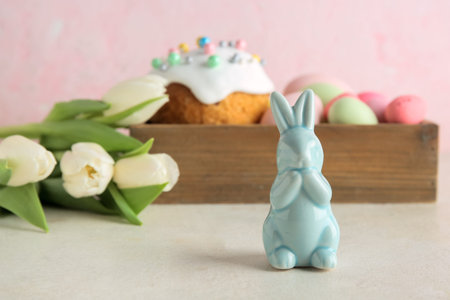 Decorative bunny, Easter eggs and cake in wooden box on gray table near pink wall